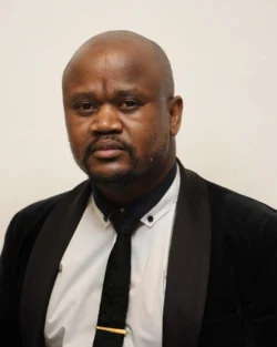A dark skinned man wearing a suit and tie